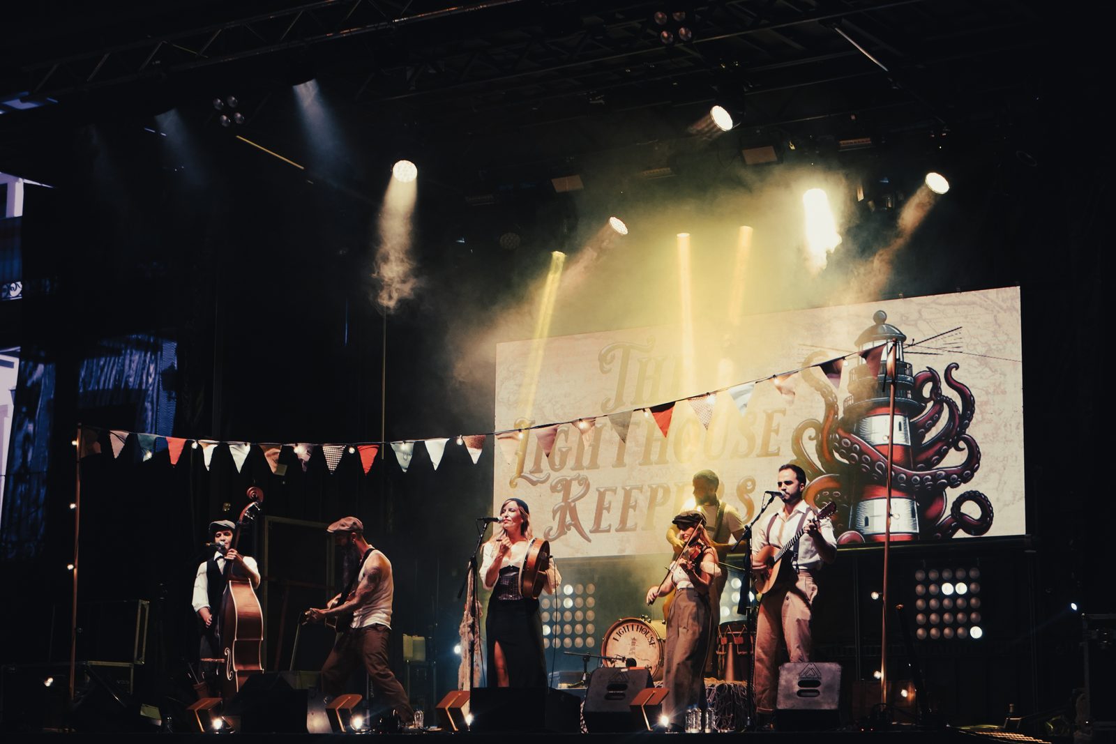 The Lighthouse Keepers tocando en un gran escenario con luces y banderines